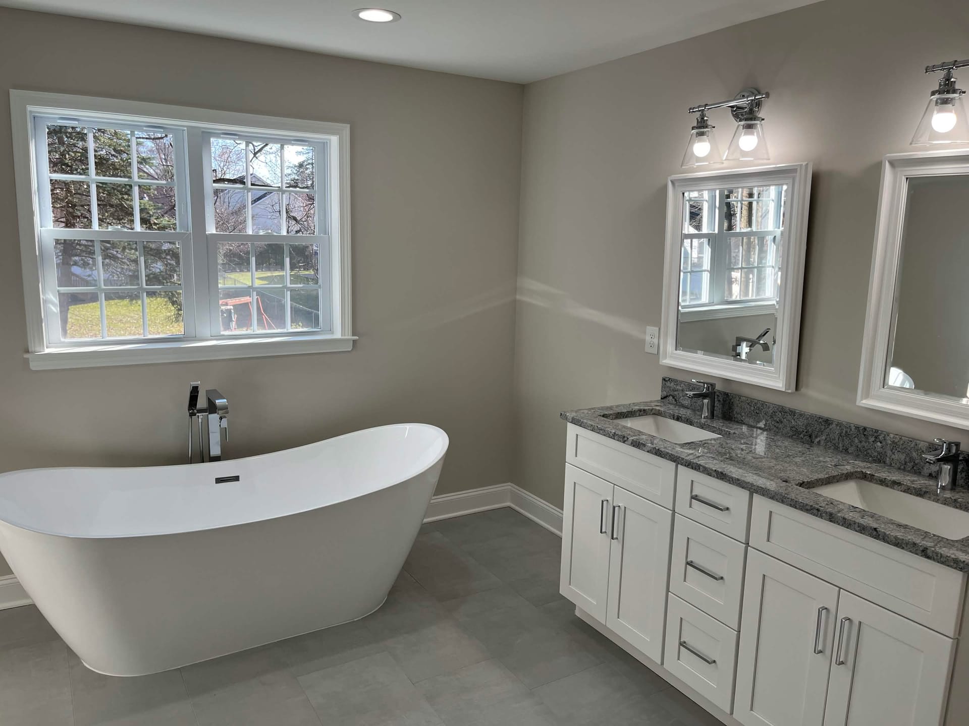 Master bathroom with freestanding soaking tub, double vanity with granite countertop, and modern lighting, built by Cursi Construction Inc.