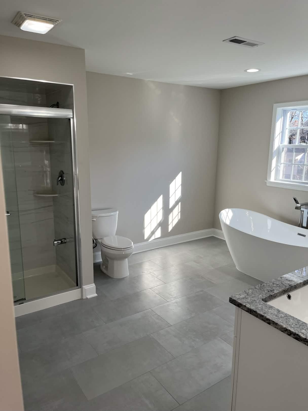 Spacious bathroom with glass-enclosed shower, freestanding tub, and granite vanity, built by Cursi Construction Inc.
