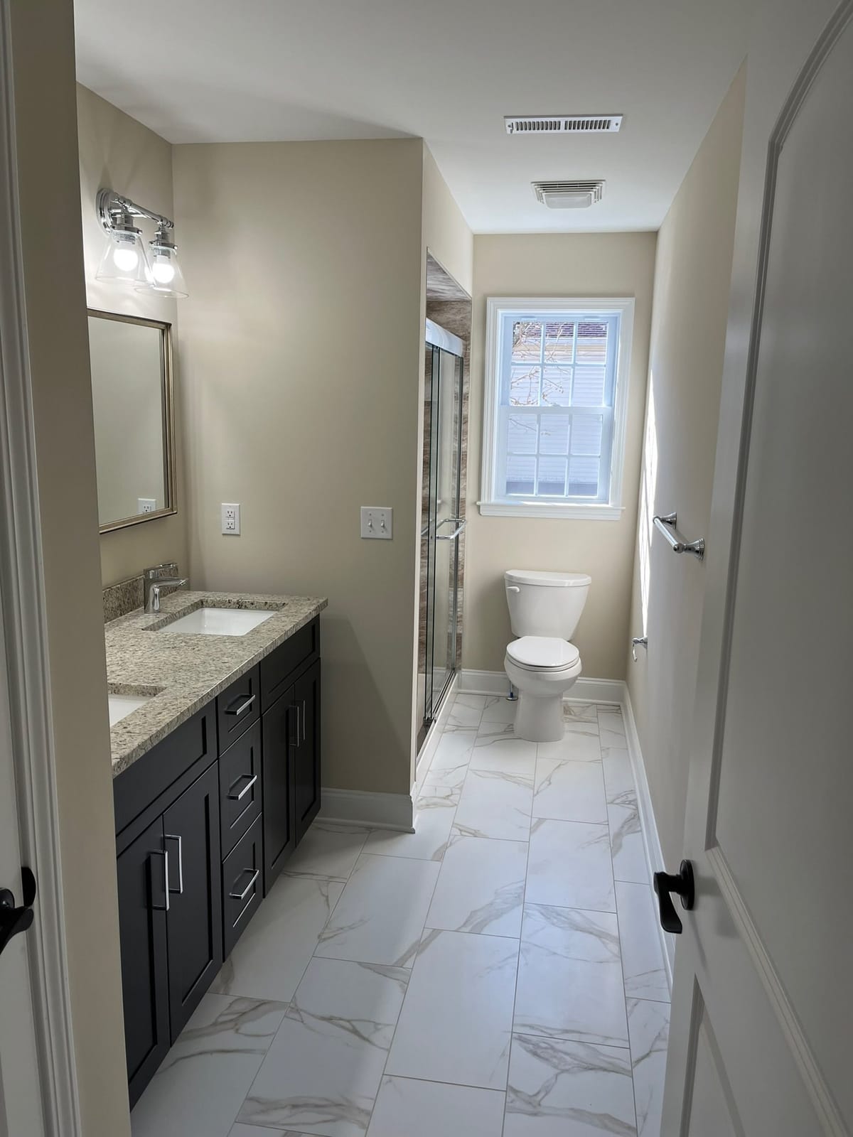 Bathroom renovation with dark vanity, granite countertop, marble-look tile floor, toilet, and window, built by Cursi Construction Inc.