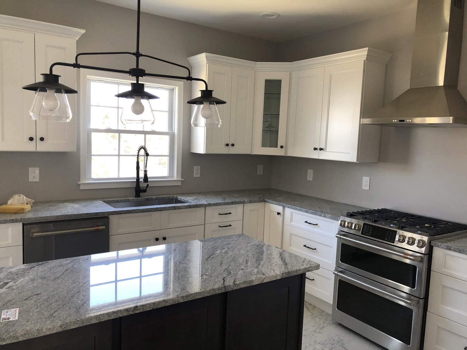 Bright custom kitchen with white shaker cabinets, granite countertops, stainless steel appliances, pendant lighting, and large island by Cursi Construction Inc.