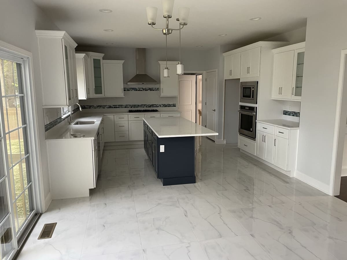 Bright kitchen renovation with white cabinetry, blue island, built-in appliances, and marble-look tile floor, built by Cursi Construction Inc.