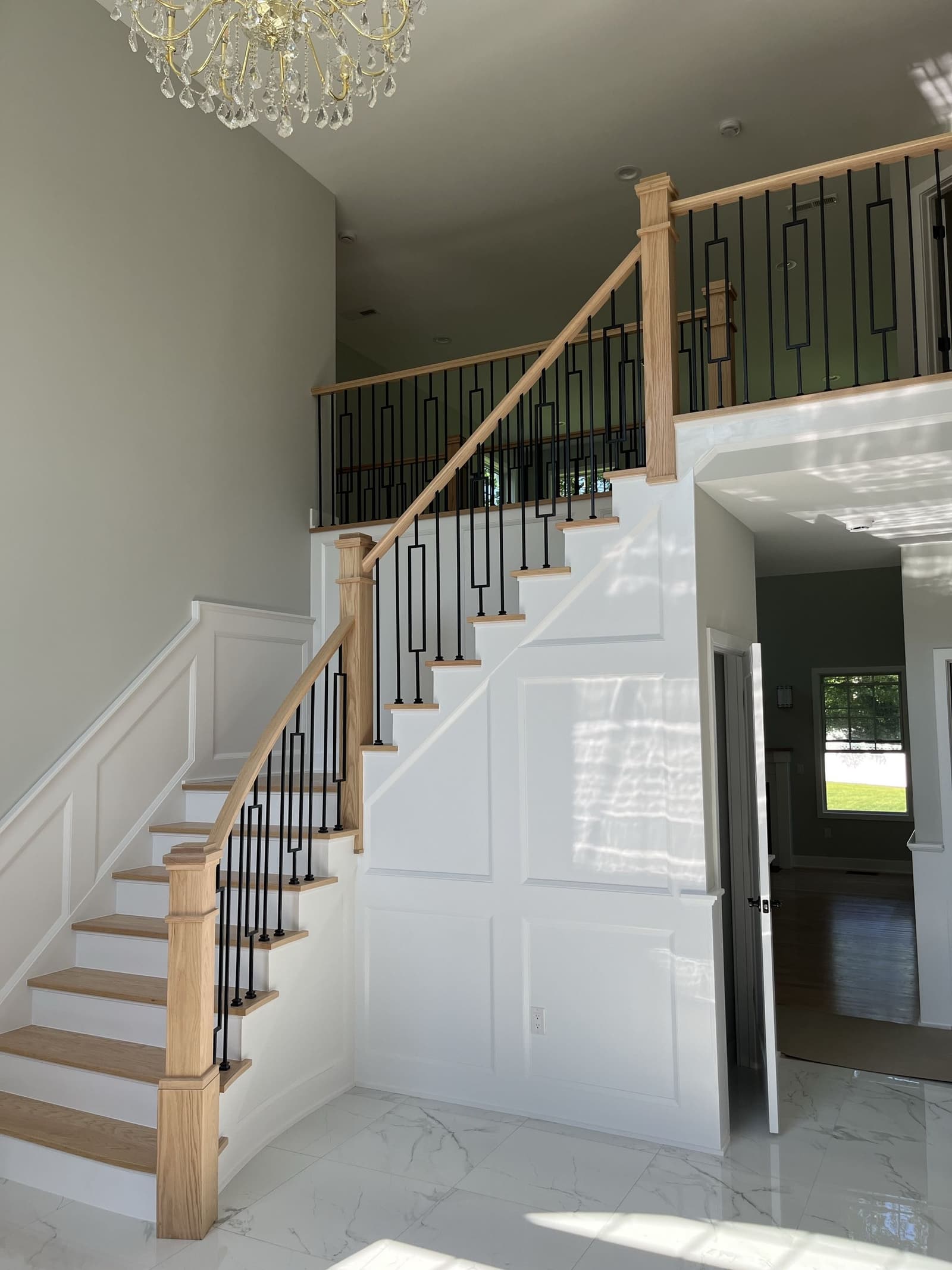 Finished staircase with natural wood handrail, black iron balusters, white panel trim, and marble-look tile floor, built by Cursi Construction Inc.