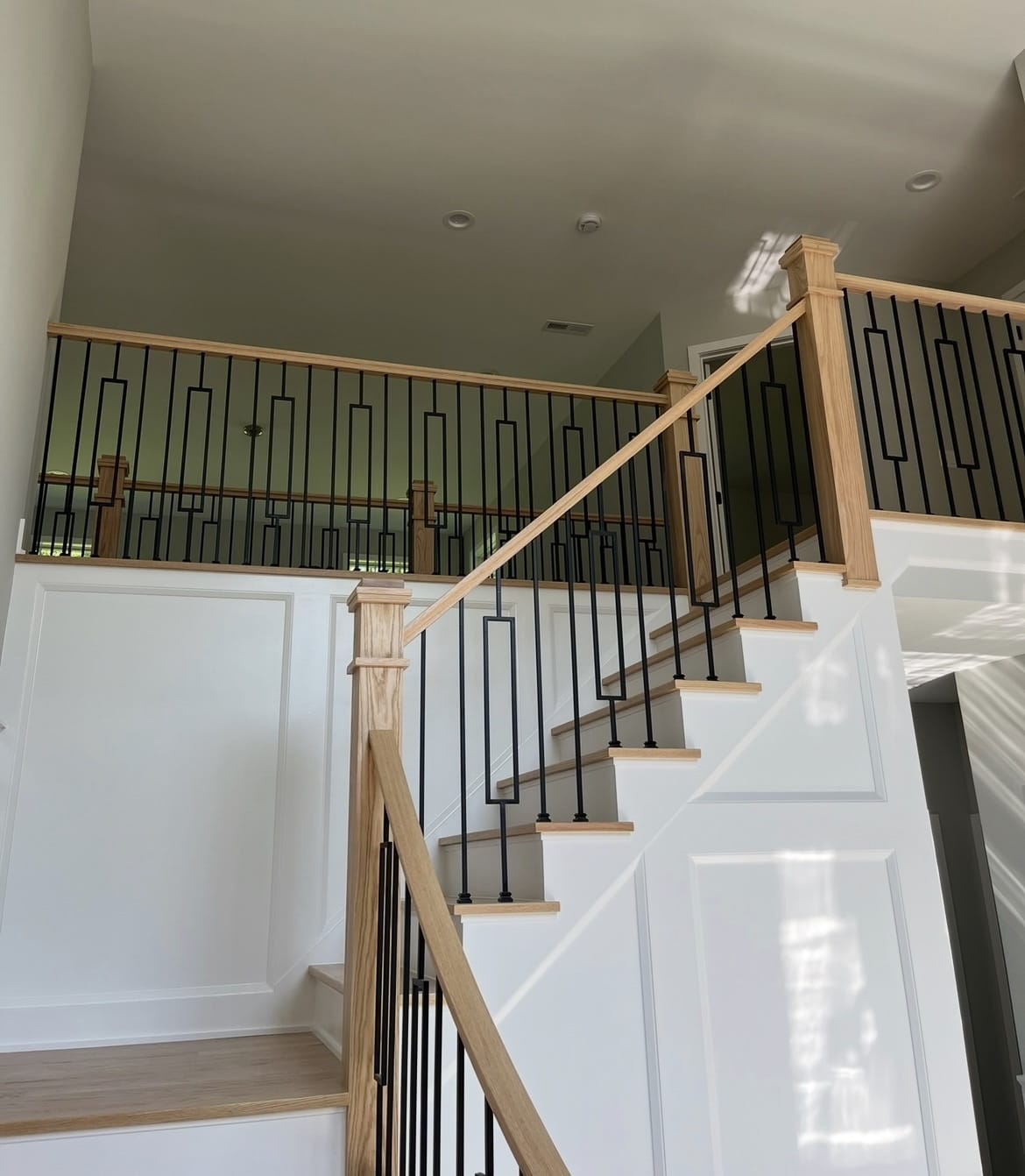 Custom staircase with wood railings, black metal balusters, white panel trim, and matching wood treads by Cursi Construction Inc.