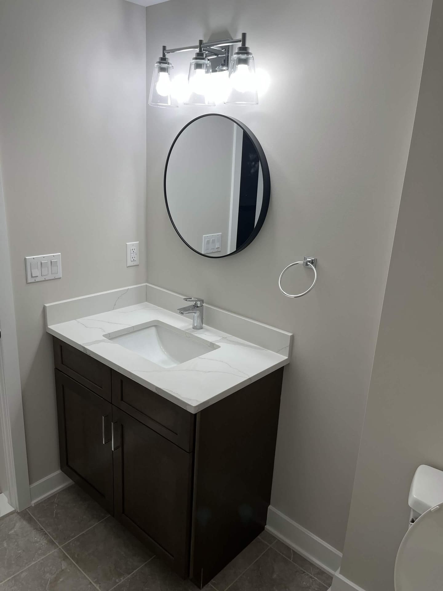 Finished basement bathroom vanity with round mirror and wall lighting by Cursi Construction Inc.