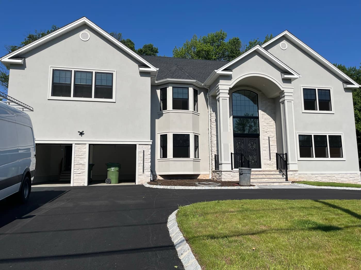 Finished custom home with stucco exterior, stone accents, black window trim, arched entry, and paved driveway, built by Cursi Construction Inc.