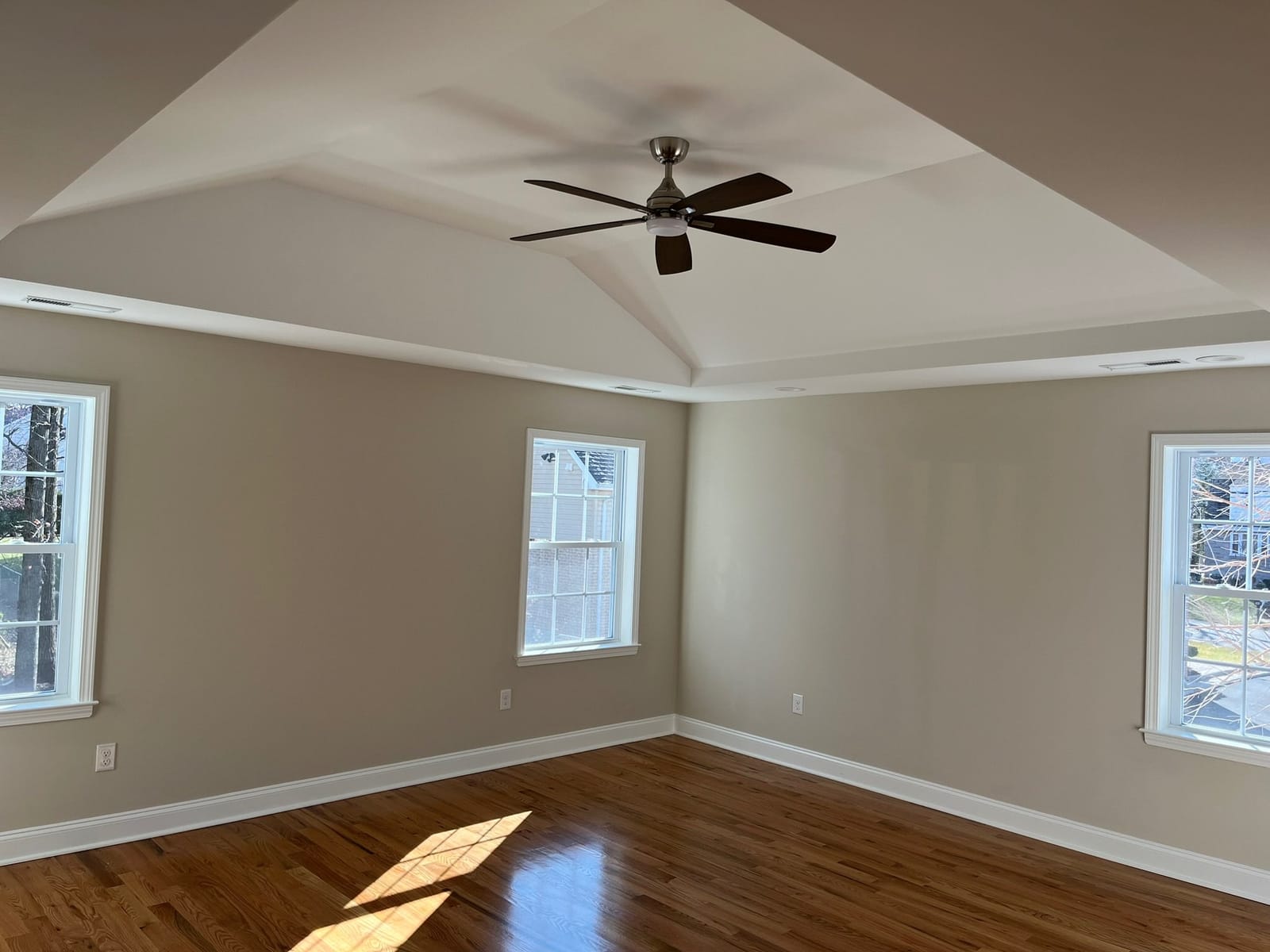 Finished room with tray ceiling, ceiling fan, recessed lighting, hardwood floors, and large windows, built by Cursi Construction Inc.