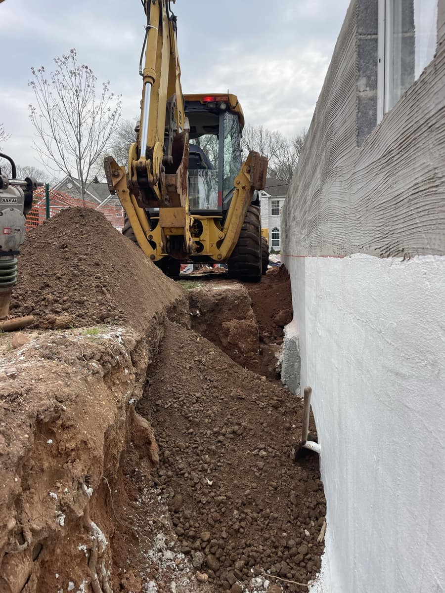 Excavator working alongside a foundation wall during residential construction by Cursi Construction Inc.
