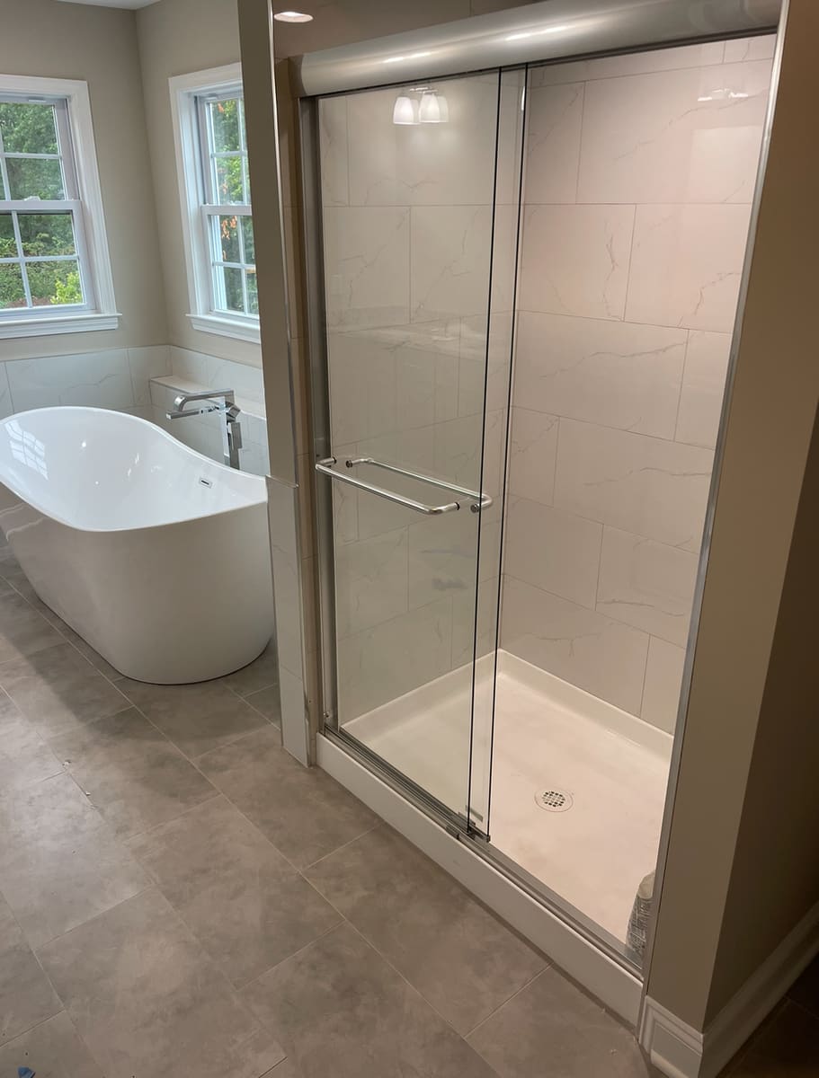 Bathroom renovation with freestanding tub, glass shower enclosure, marble-look shower tile, and gray floor tile, built by Cursi Construction Inc.