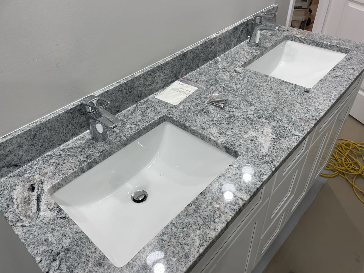 Close-up of double vanity with granite countertop, undermount sinks, chrome faucets, and gray cabinetry by Cursi Construction Inc.
