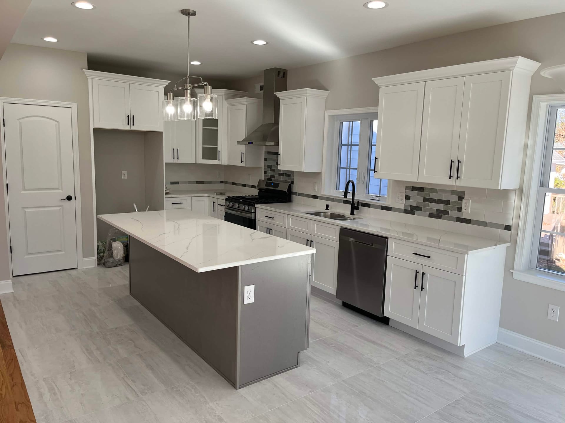 Modern kitchen with white shaker cabinets, quartz island countertop, mosaic backsplash, and stainless steel appliances, built by Cursi Construction Inc.