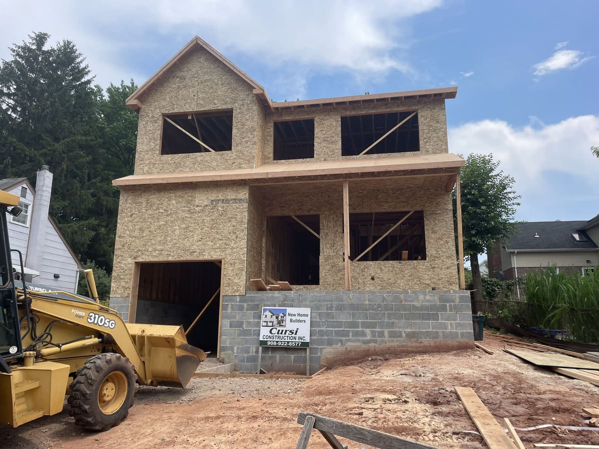 New home under construction with block foundation, wood framing, porch roof, and construction equipment by Cursi Construction Inc.
