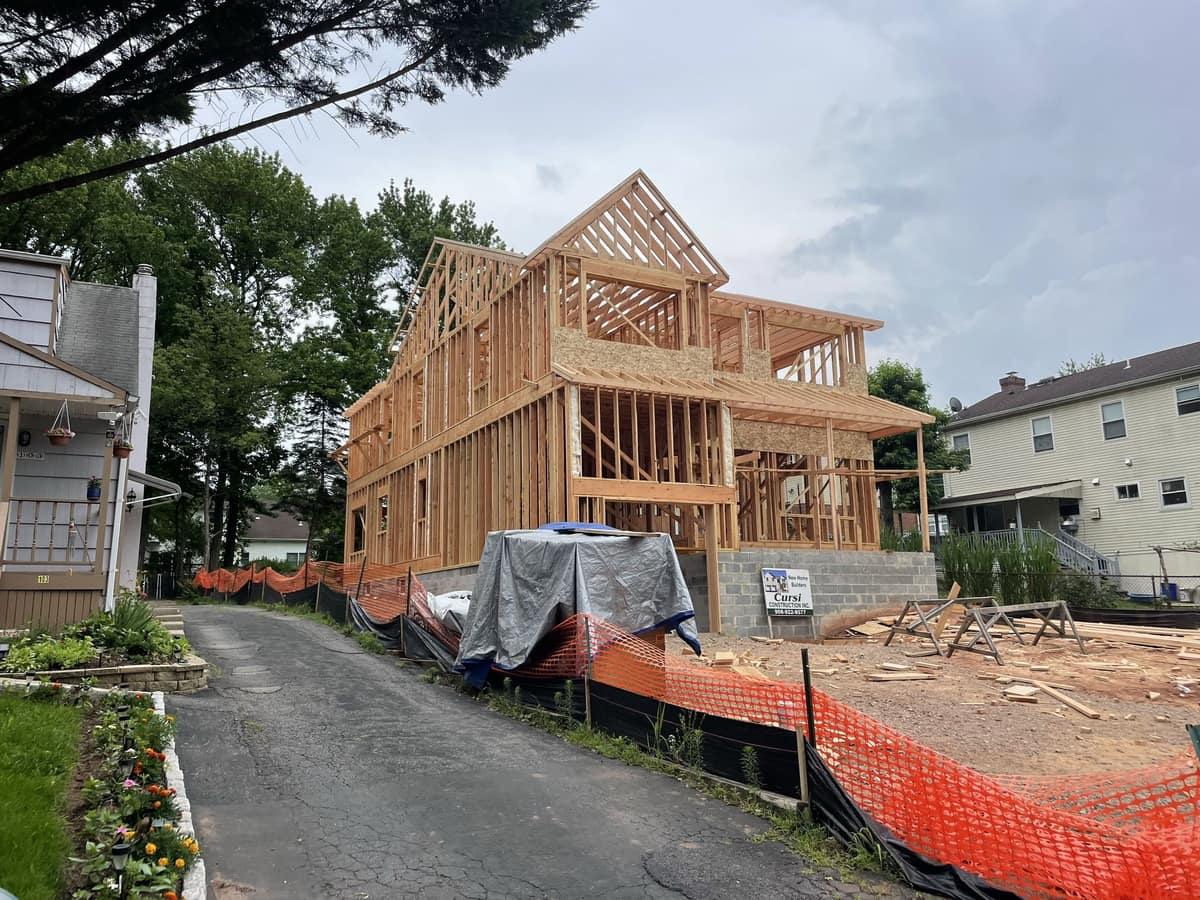 Side view of a new home under construction with wood framing and construction materials by Cursi Construction Inc.