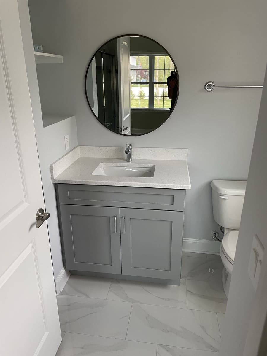 Powder room renovation with gray vanity, round mirror, white countertop, and neutral tile floor, built by Cursi Construction Inc.