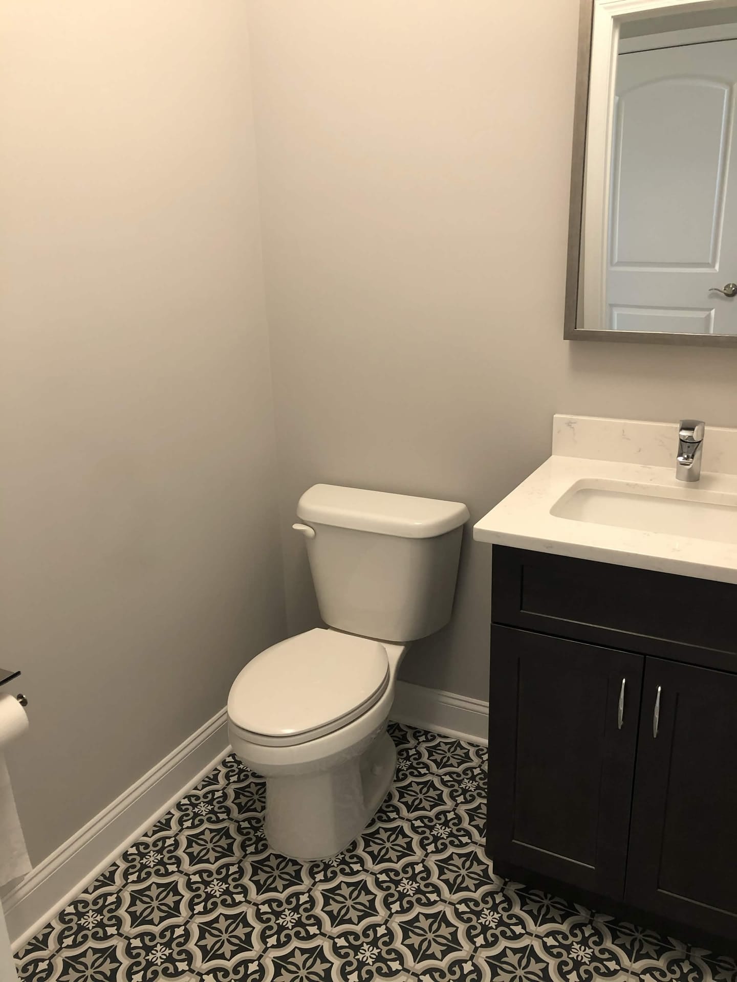 Renovated powder room with patterned tile floor, dark vanity, white countertop, chrome faucet, and gray walls, built by Cursi Construction Inc.