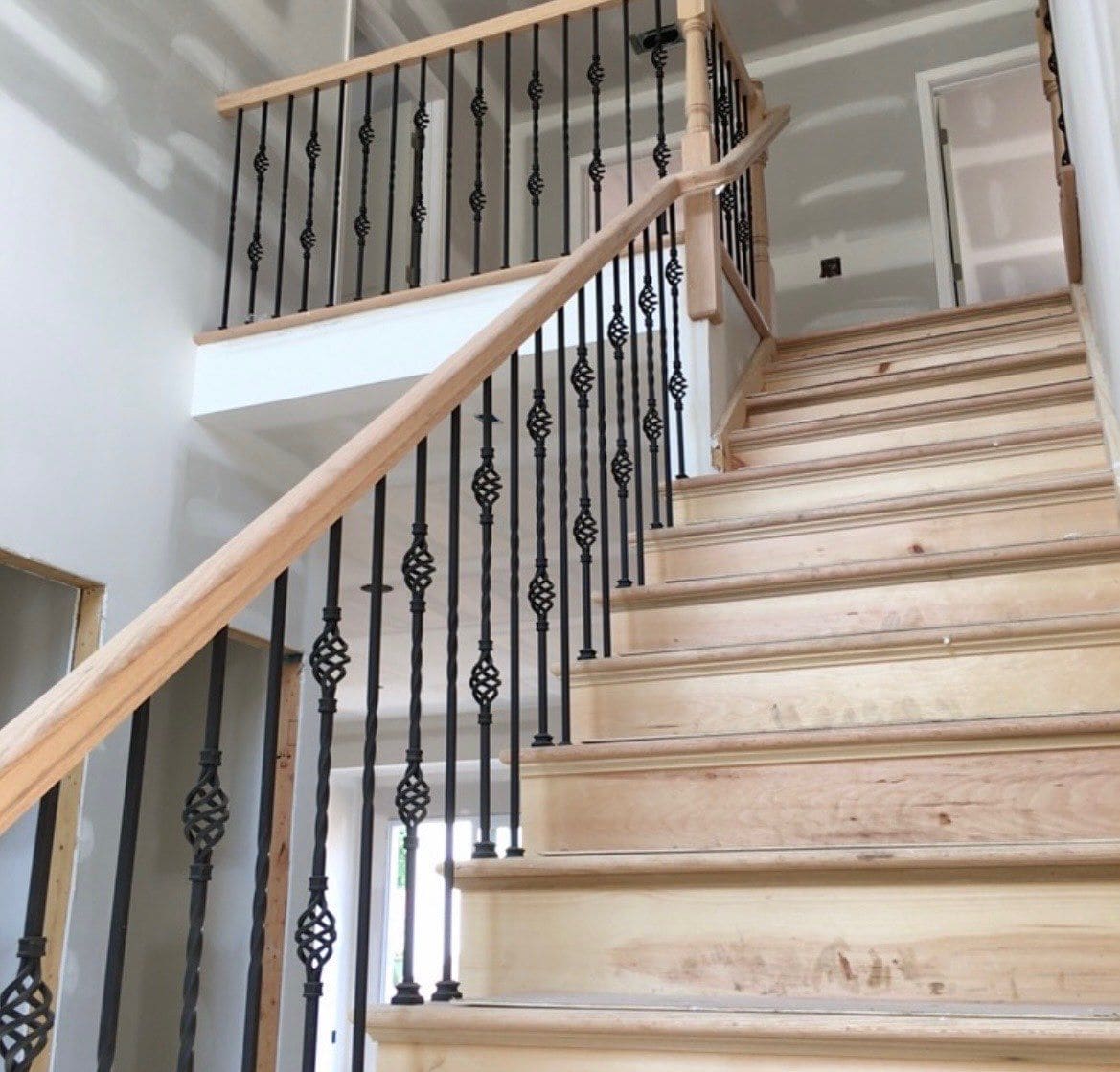 Unfinished staircase with wood railings and decorative black iron balusters during construction by Cursi Construction Inc.
