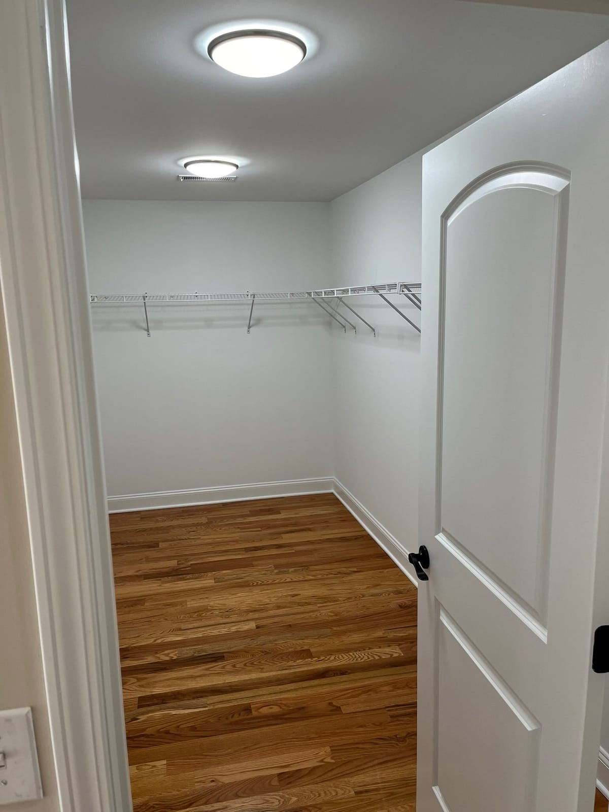 Finished walk-in closet with hardwood floors, white storage shelving, painted walls, and interior door, built by Cursi Construction Inc.