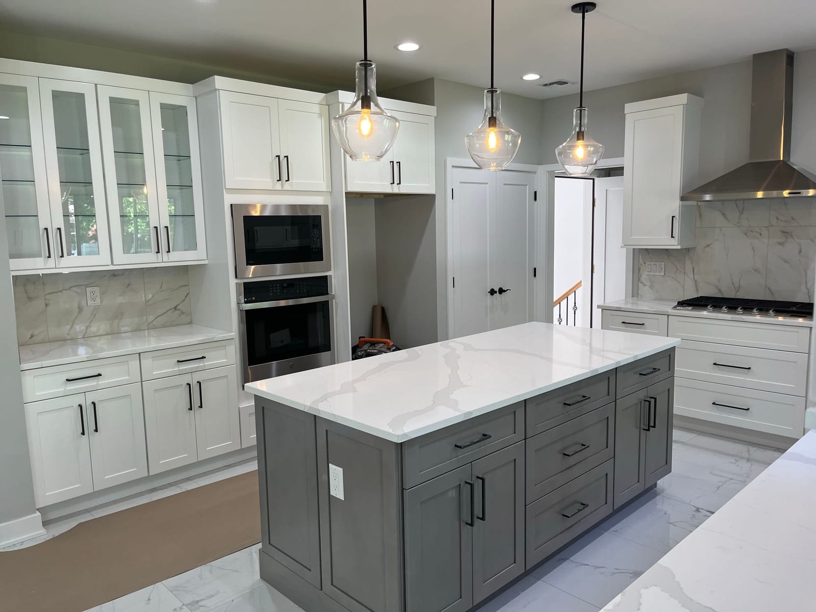 White kitchen renovation with gray island, glass pendant lights, white cabinetry, marble-look backsplash, and stainless appliances, built by Cursi Construction Inc.