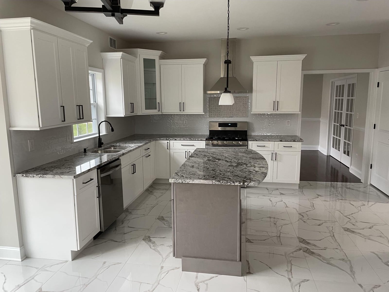 Renovated kitchen with white cabinets, granite counters, island, stainless range hood, and marble-look tile floor, built by Cursi Construction Inc.